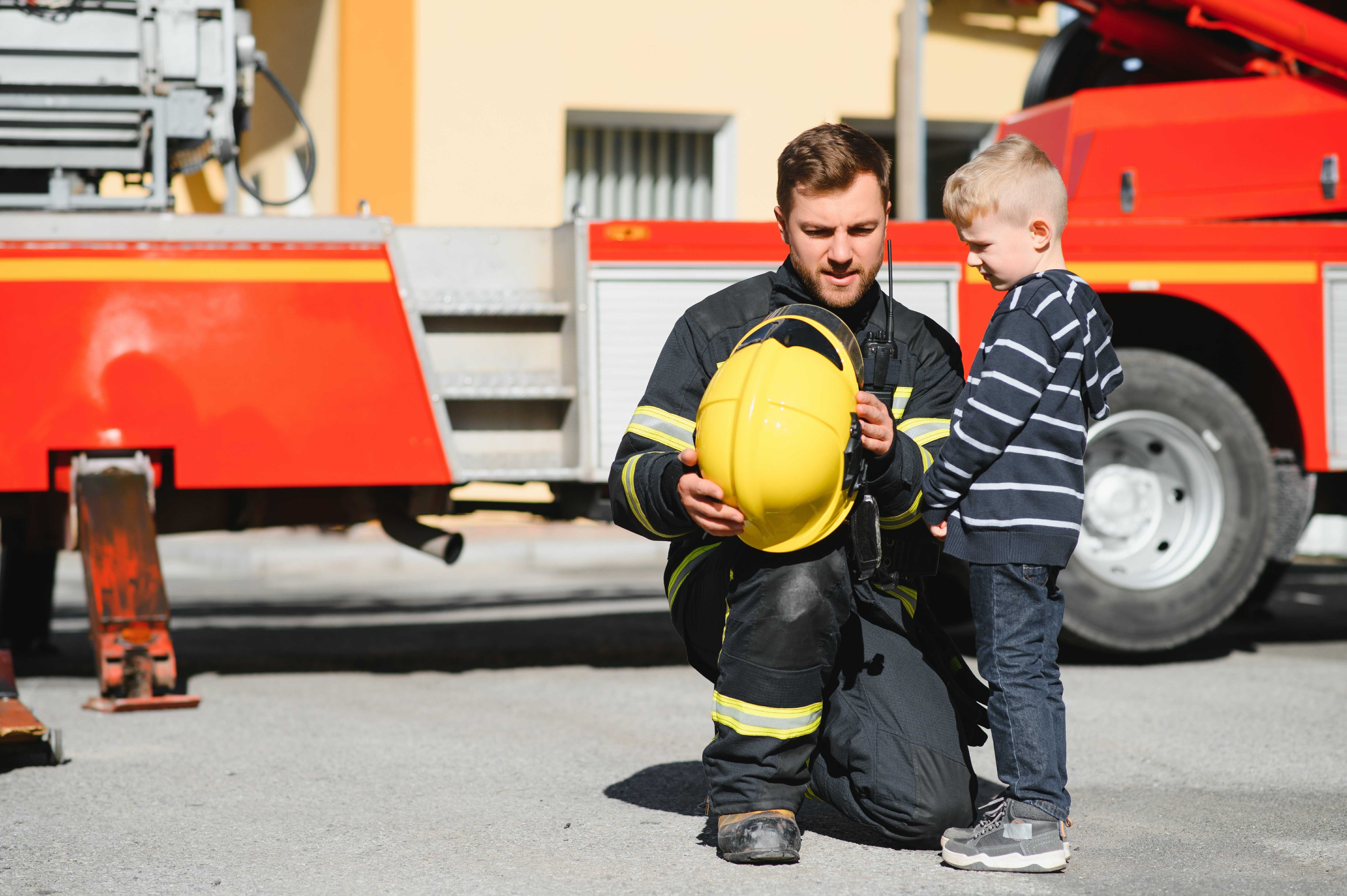 A firefighter showing his helmet to a young boy in front of a fire truck